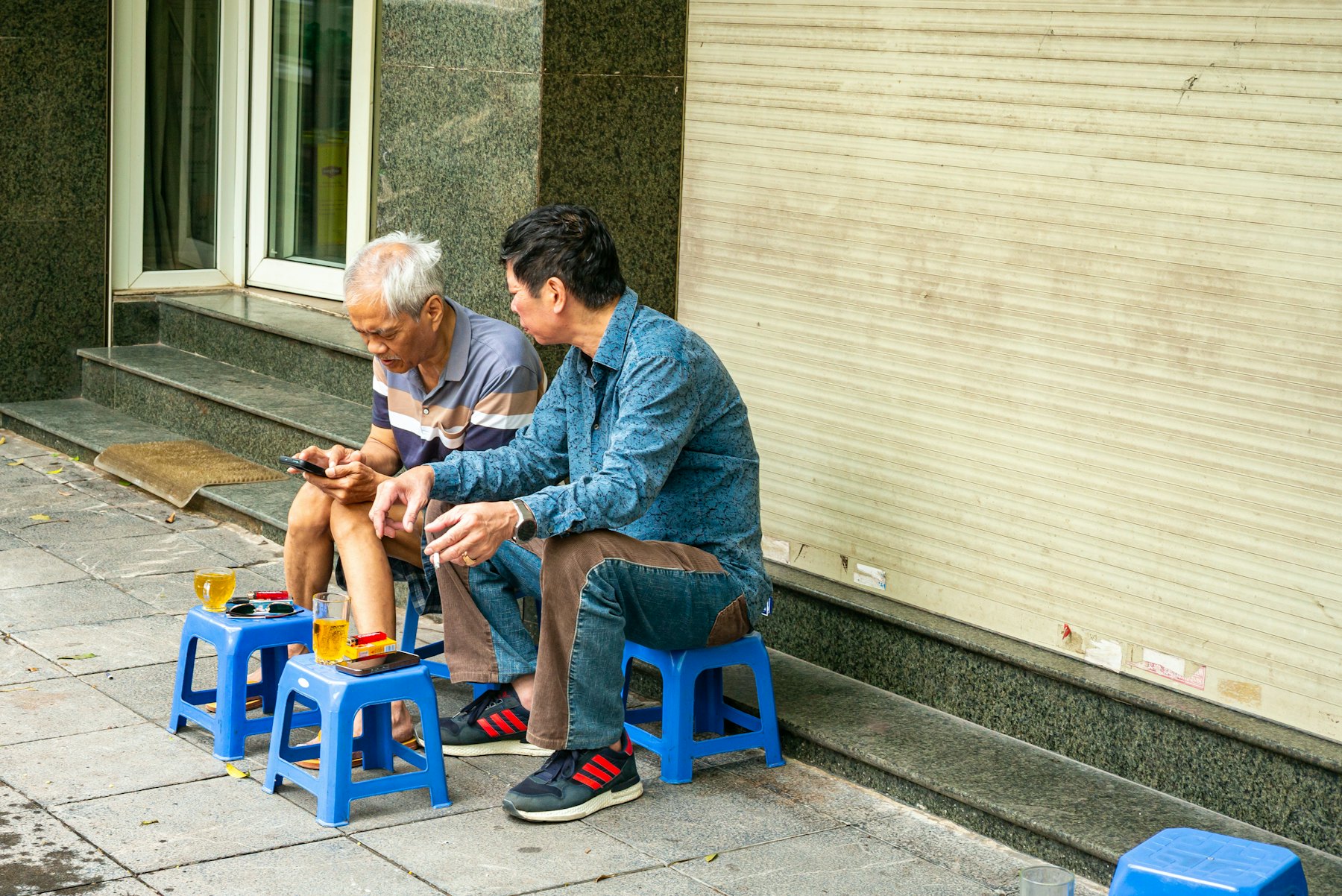 Two elderly men chatting over tea on stools