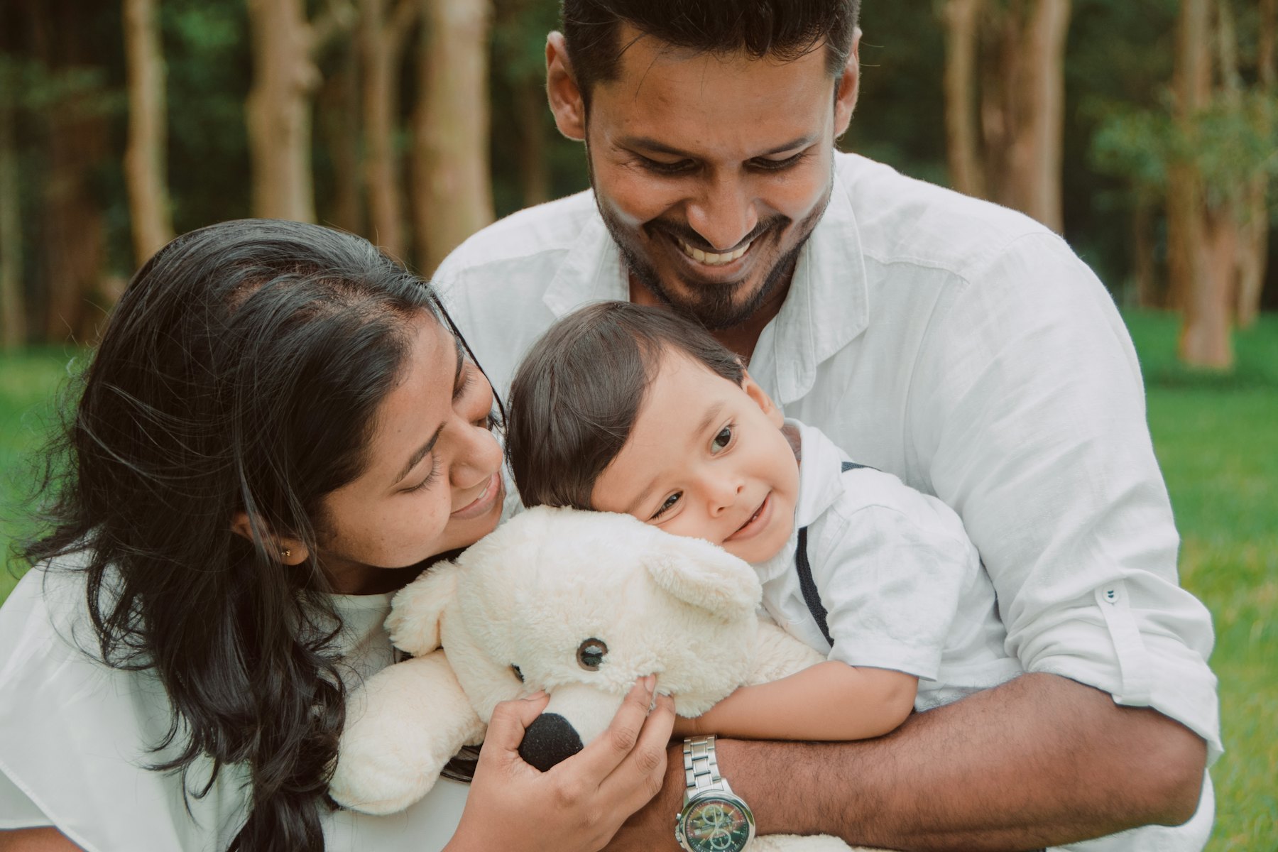 Parents cuddling their baby with a teddy bear