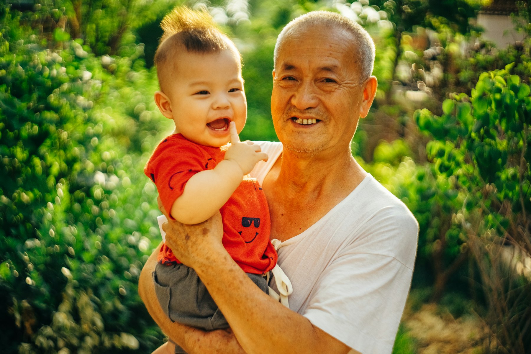 Grandfather carrying his laughing baby grandson in a garden