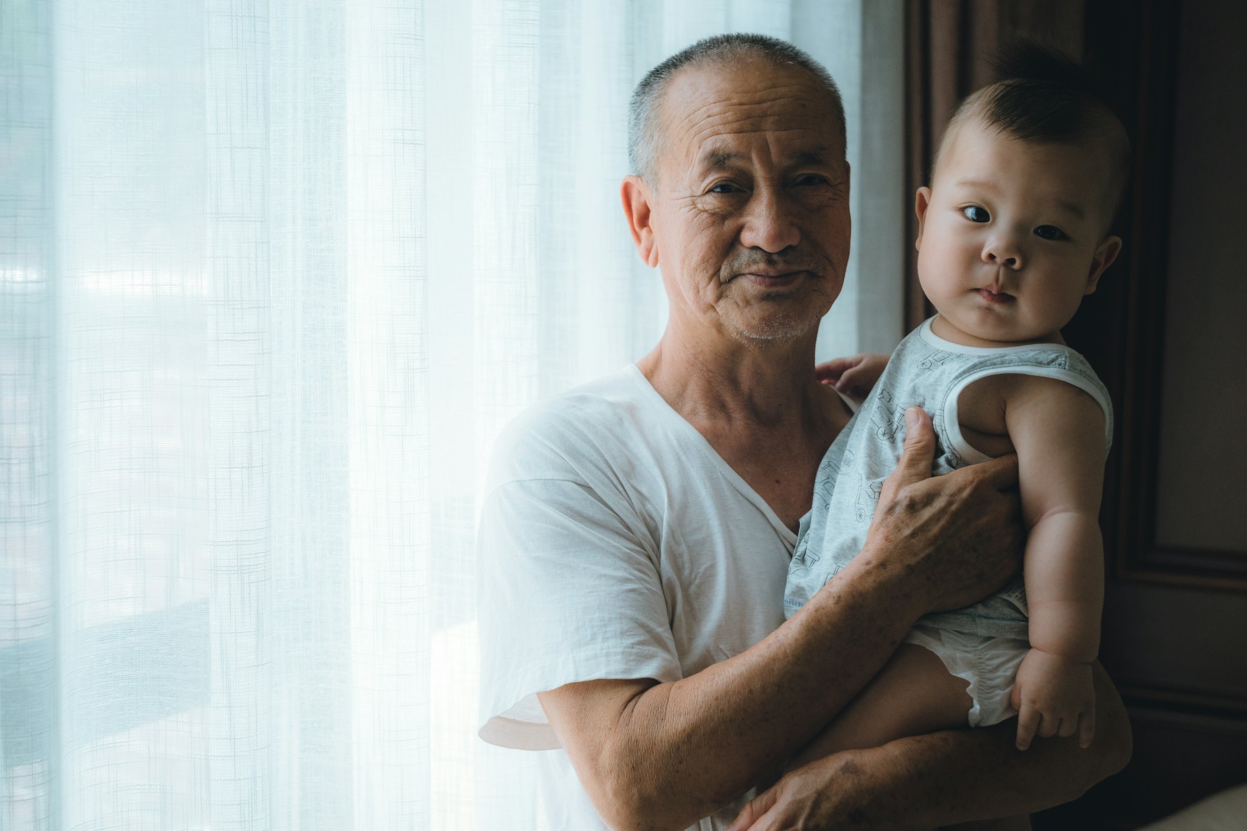Grandfather holding his baby grandson by the window