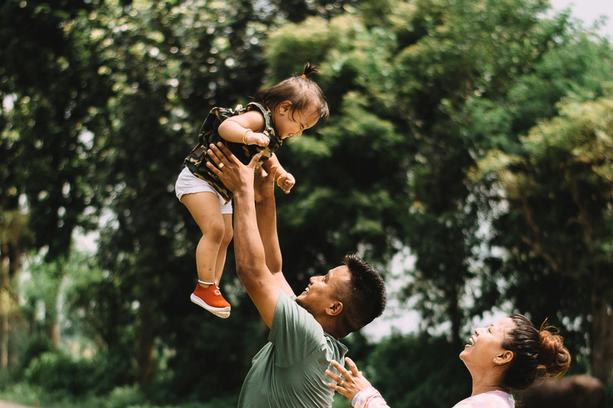 Father lifting his laughing baby in the air as the mother looks on
