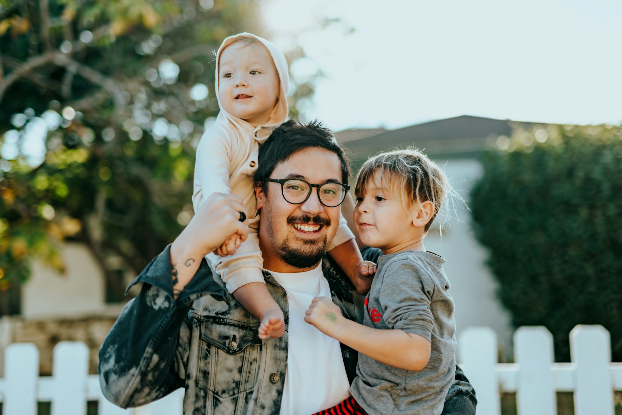 Smiling father carrying his two young children outside their home