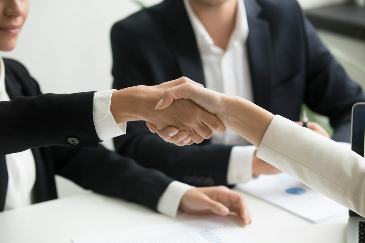 Two people shaking hands over a signed agreement