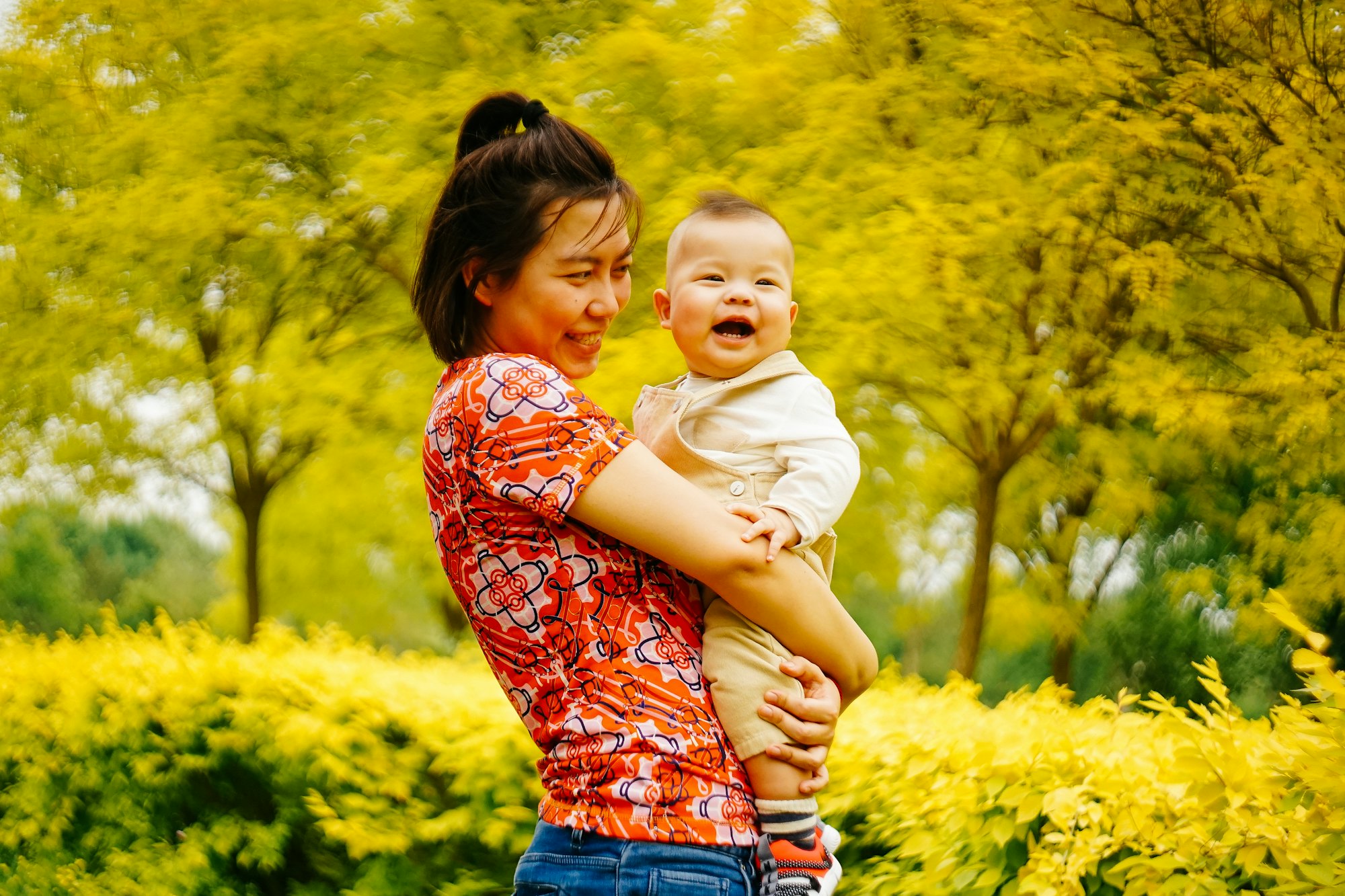 Malaysian mother holding her laughing baby in a sunny park