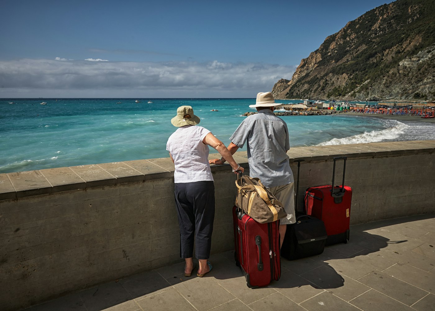 Retired couple with suitcases looking out to sea on holiday